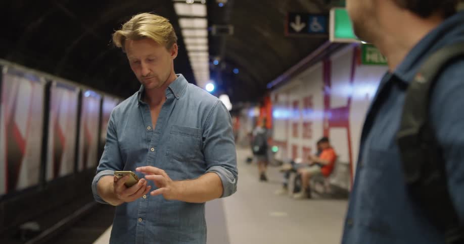 Man stands near empty tracks in train station checking his mobile phone