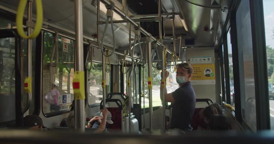A man wearing mask is travelling in a public bus while standing