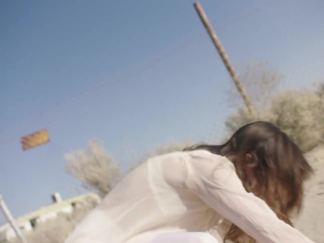 A woman repeatedly falls in the sand as she moves forward