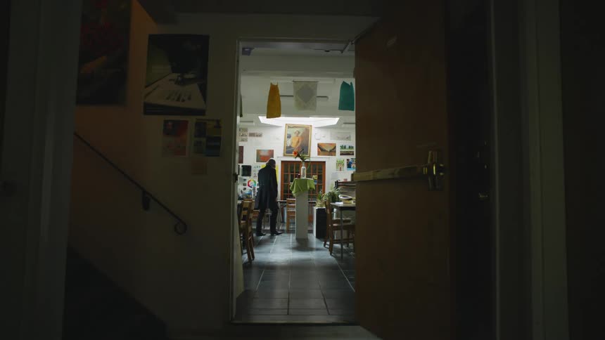An open classroom door shows an art teacher setting up a flower jar on a podium