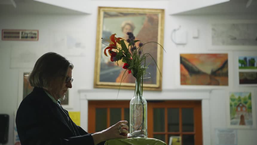 A man places flowers in a vase in an art classroom