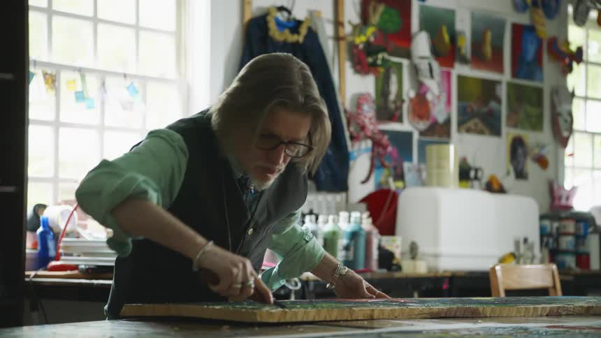 A man in a workshop using a tool to carve into a piece of wood