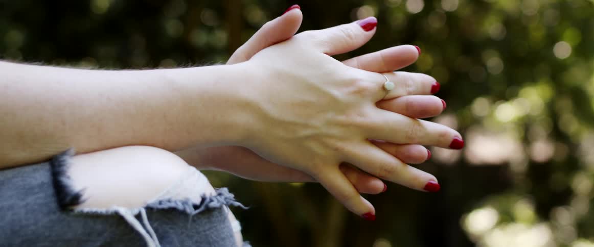 A woman with rings on her fingers with trees and leaves in the background