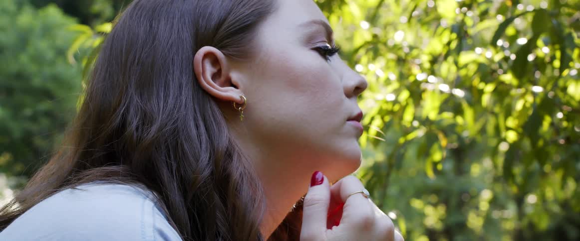 A woman with makeup outside with trees and leaves in the background