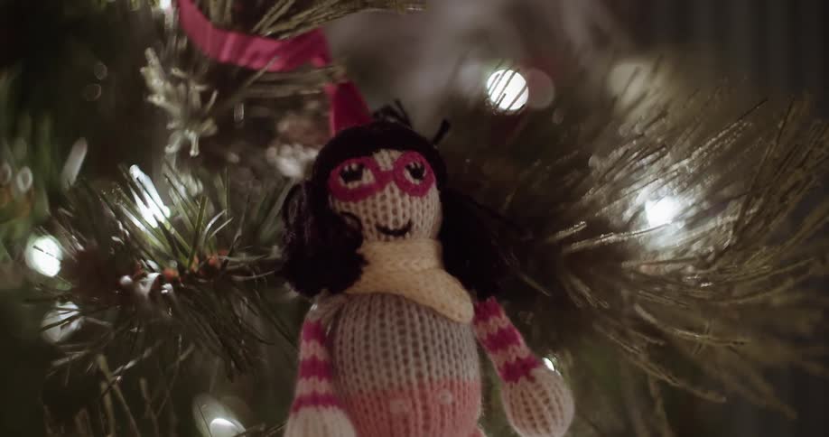 A small doll christmas ornament hanging on a christmas tree