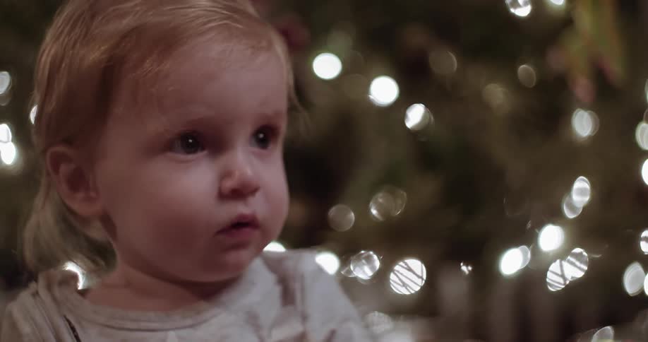 A child is looking forward near a christmas tree