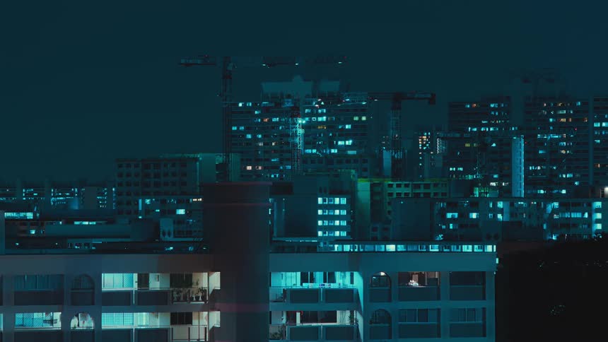 Lights come on an off in building as construction cranes move over construction site at night