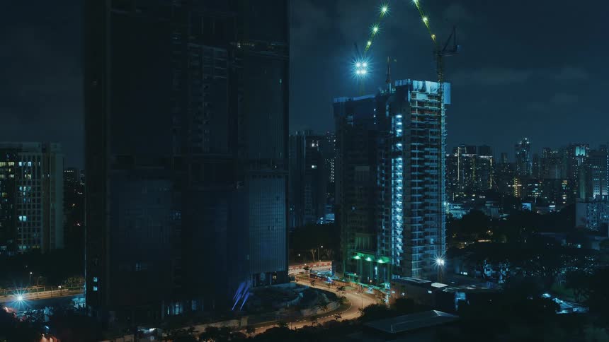 Construction crews use cranes while working on a skyscraper at night
