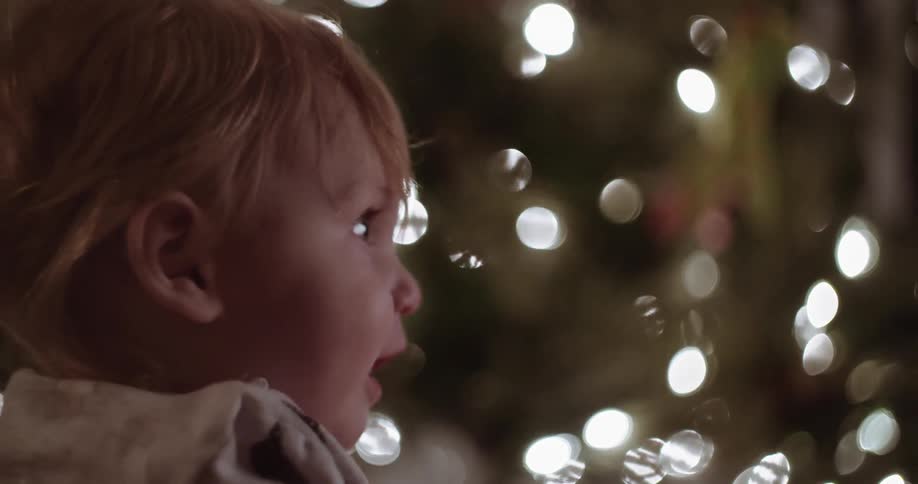 A baby sits near a christmas tree and looks around
