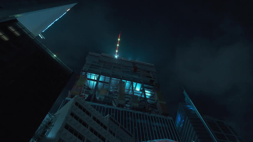 Building under construction grows as construciton cranes move and clouds pass over head at night