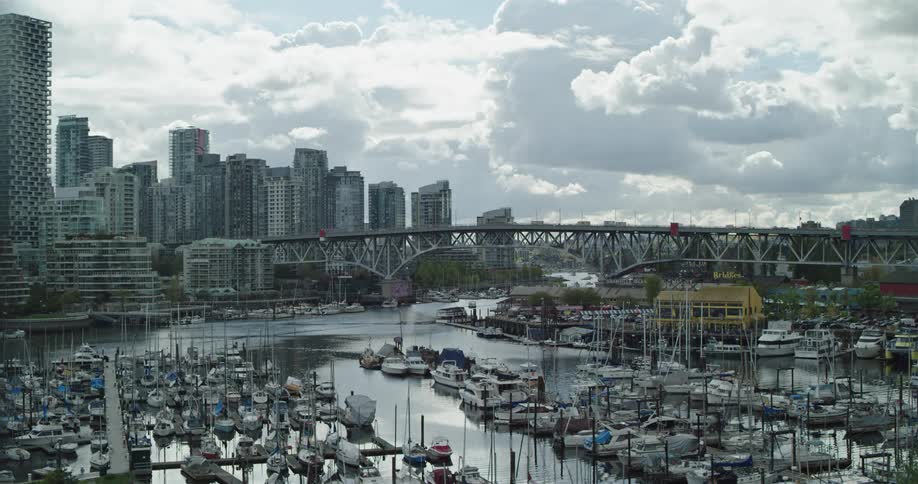 Numerous boats are docked at a marina located next to a metropolitan area in Vancouver