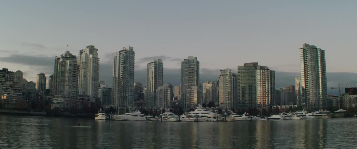 A person kayaks in the waterway past downtown and docked boats in a marina