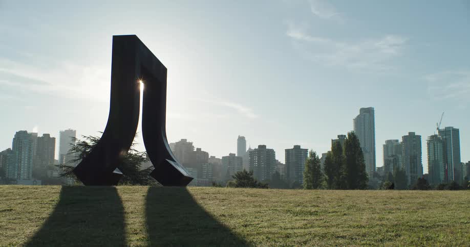 A large metal sculpture casts a shadow on the grass nearby