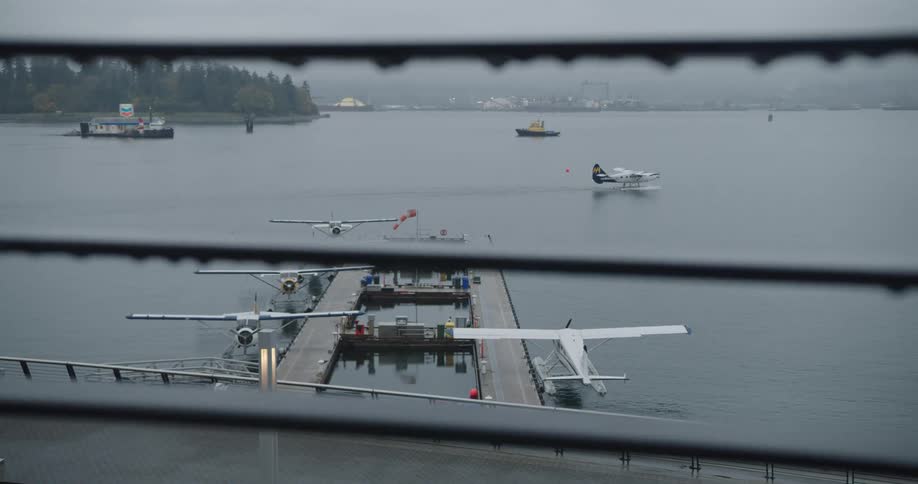 Dense fog covers distant shore as boats and seaplanes move across water near pier