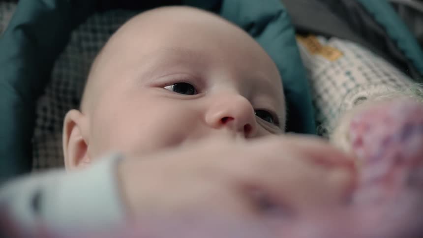 A baby laying in a car seat holds its blanket