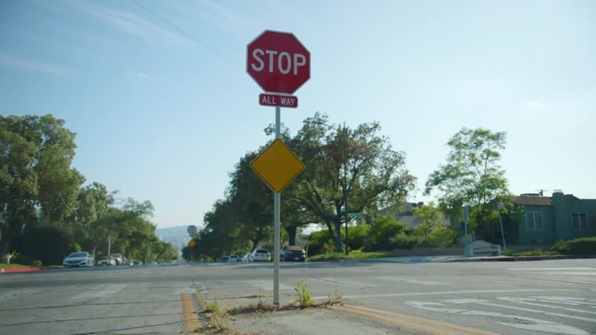 All way stop sign sits at an intersection while trees stand nearby