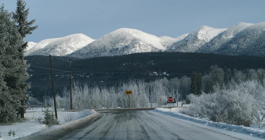 A road covered in snow with trees a mountain range the sky and clouds in the background
