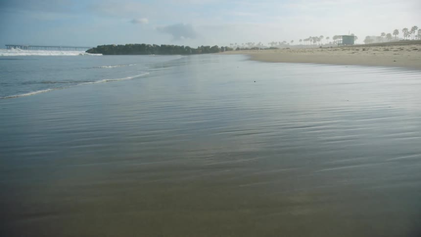 Waves gently wash ashore at a sandy beach on a pleasant sunny day