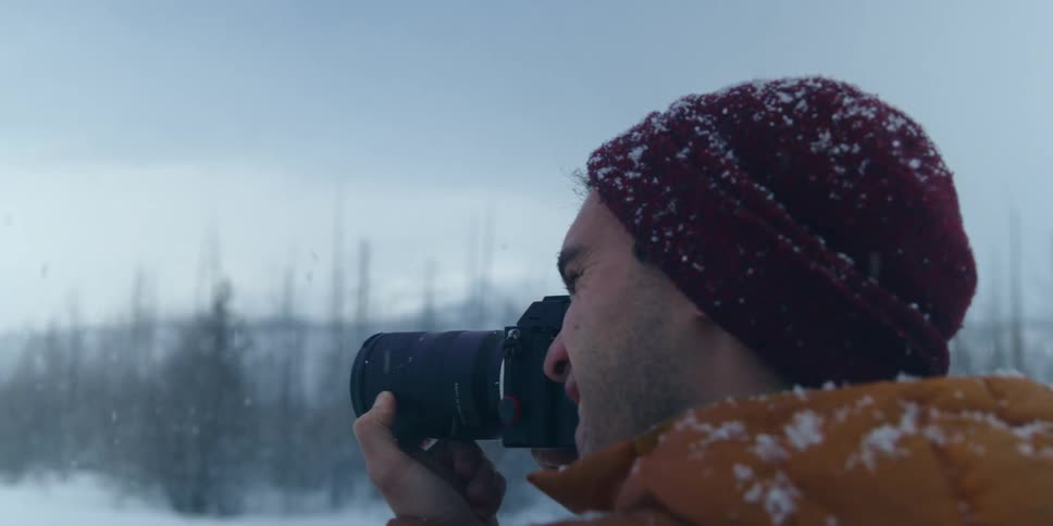 A man smiles as he takes a photograph during snowfall