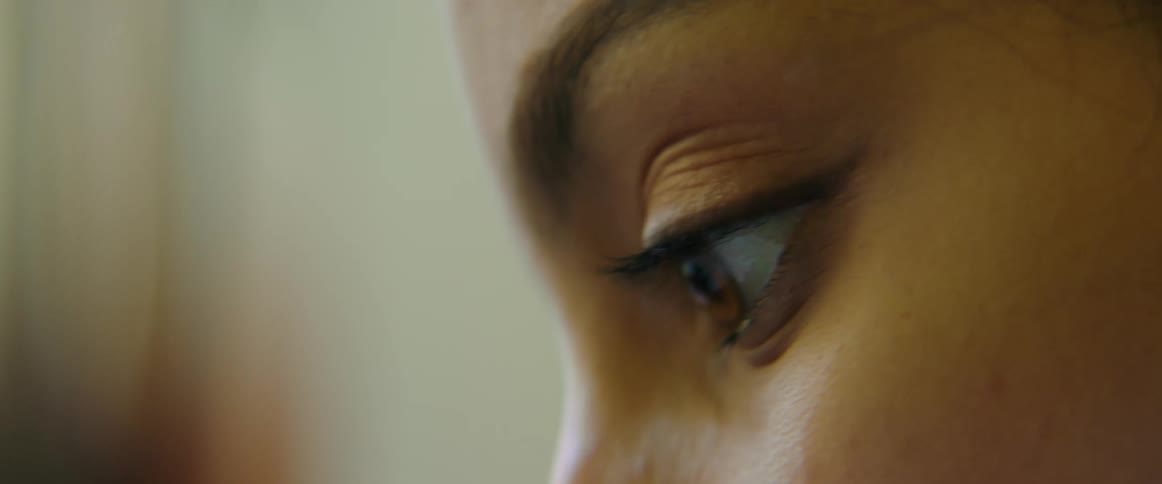 A woman in a room looking downward with a wall in the background