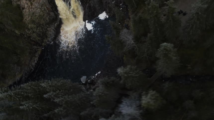 A waterfall rushes over a cliff and into a river winding through a forest