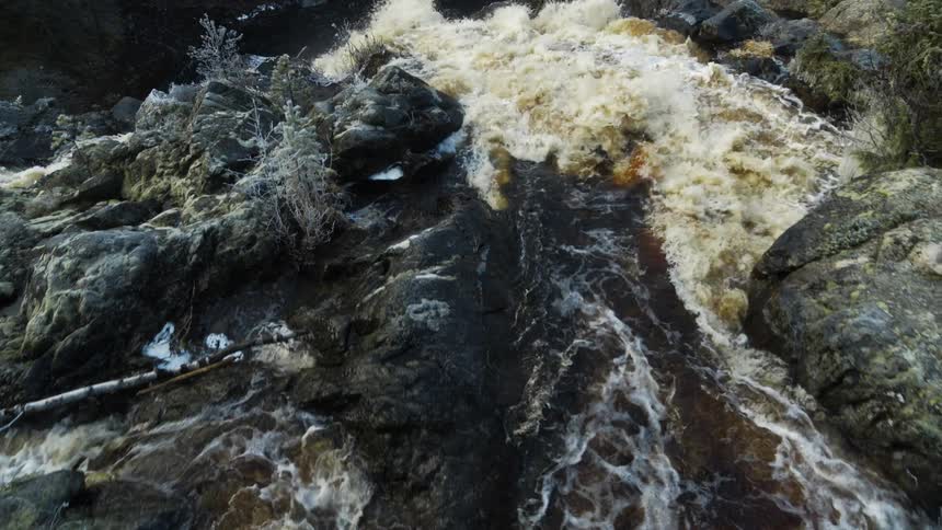 The water in the river flows near the rocks then goes down a hill