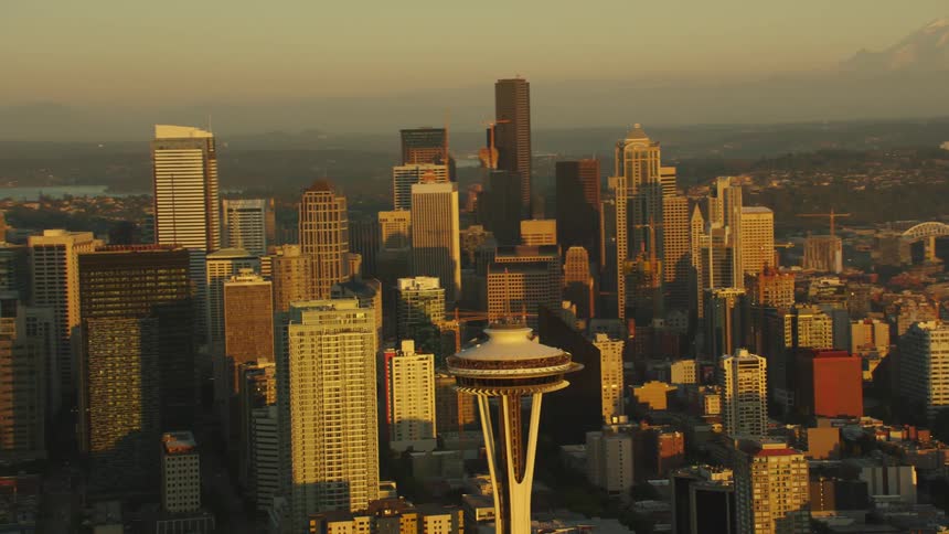 Skyscrapers sit in the city near the lake as mountains sit in the distance