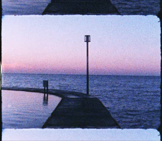 Paved walkway separates pond from ocean as sun sits on horizon in red sky