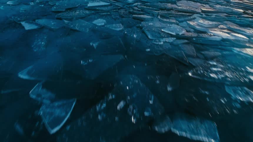 Frozen and cracked sections of ice on the surface of the ocean stack upon each other like scales