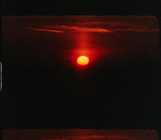 The sky is black and red as the sun sets over the ocean