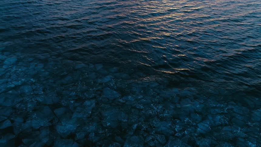 Rippling waves reflecting sunshine run into floating ice