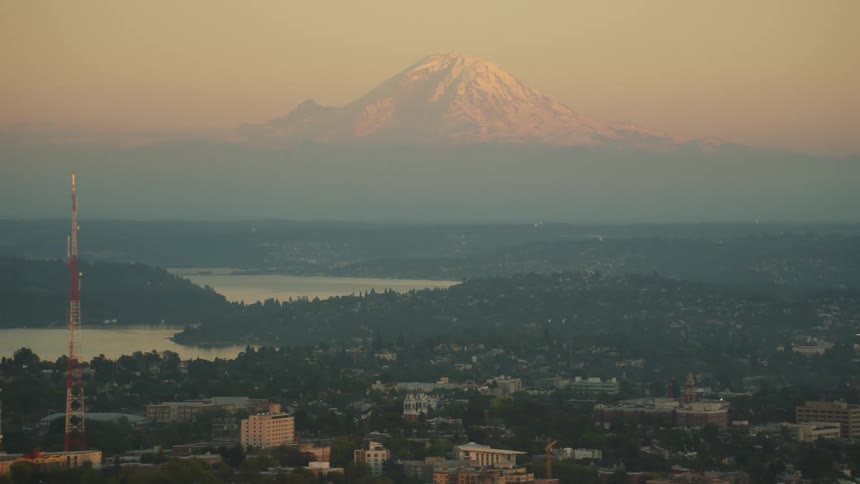 A city with buildings and trees with a mountain range the sky and clouds in the background