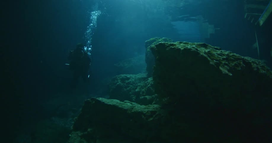 A scuba diver is swimming past rocks