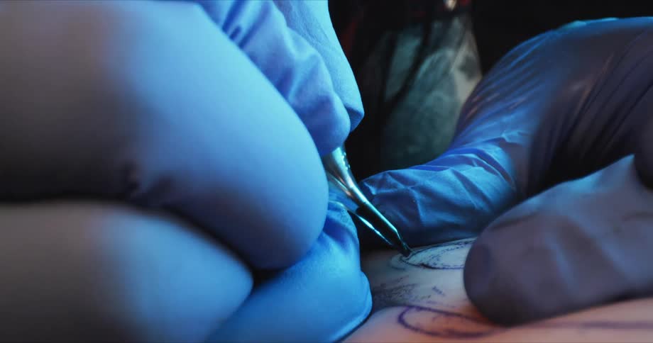 A tattoo artist uses a tattoo gun to draw a tattoo on an arm