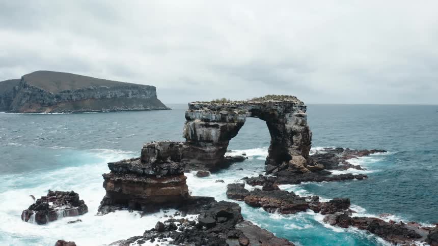 Waves splashing against a natural arch rock formation under a cloudy sky