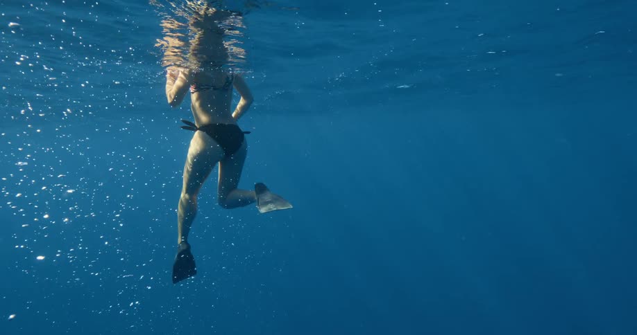 Woman with bikini and black training fins swims in the sea