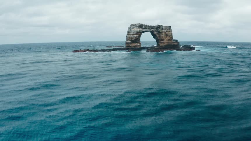 Waves splashing against a natural arch rock formation under a cloudy sky