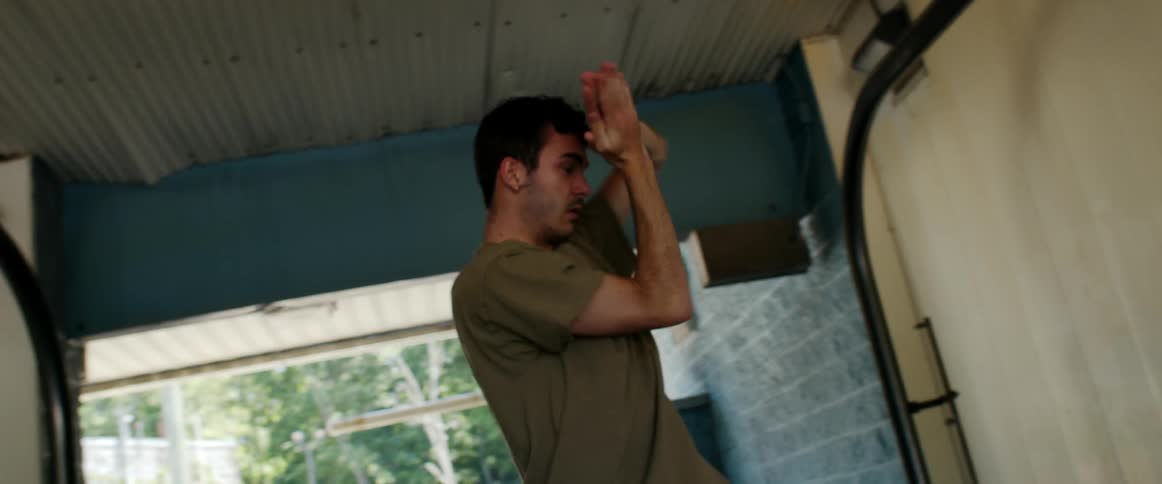 A young man looks into the camera as he dances in a garage on a sunny day