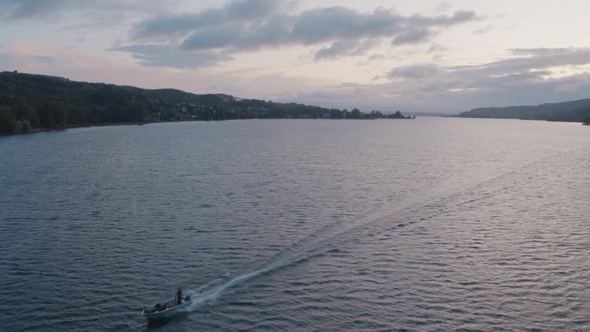 A boat speeds across a lake on a cloudy day creating waves