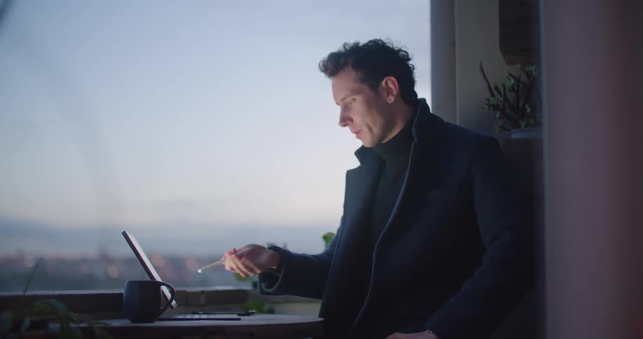 A man stands at a table tapping a tablet computer and talking at the same time