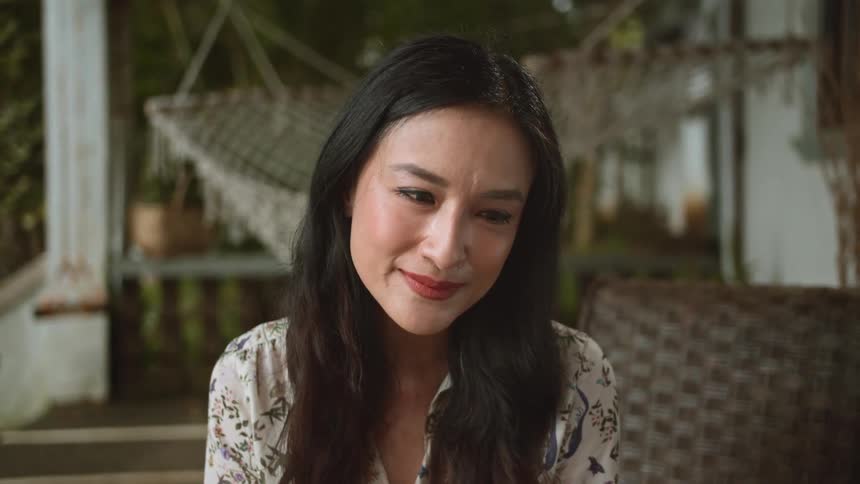 A woman smiles and wipes a tear away from her eye while sitting outdoors on her patio