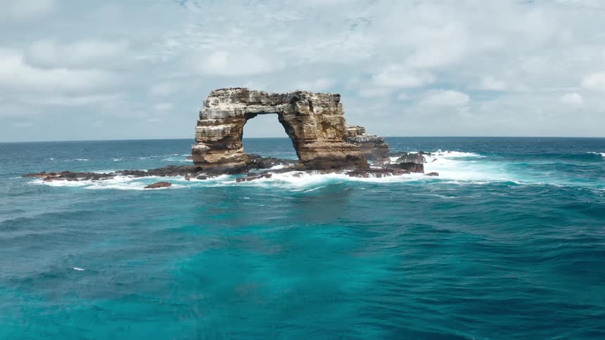An islet in the ocean surrounded by water with the sky and clouds in the background