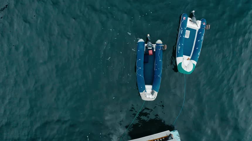 Two dinghies with motors are tied by rope to the back of a boat