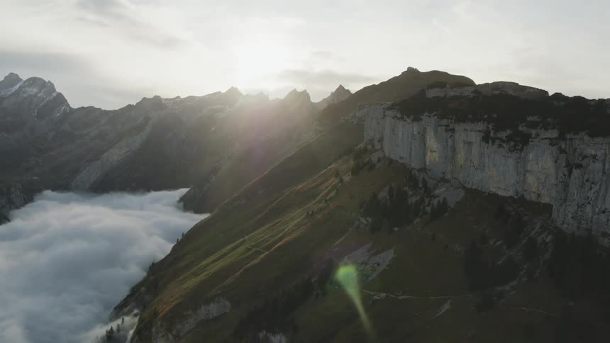 Snow covered mountain peaks high in the sky with the sun shining through the clouds