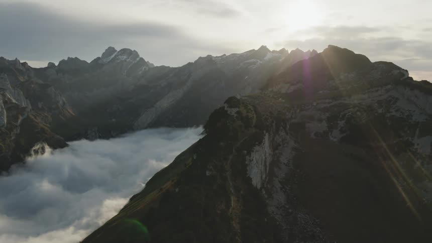 Snow covered mountain peaks high in the sky with the sun shining through the clouds