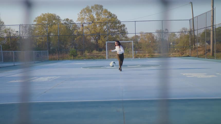 Female athlete practices taking shot in soccer on fenced court
