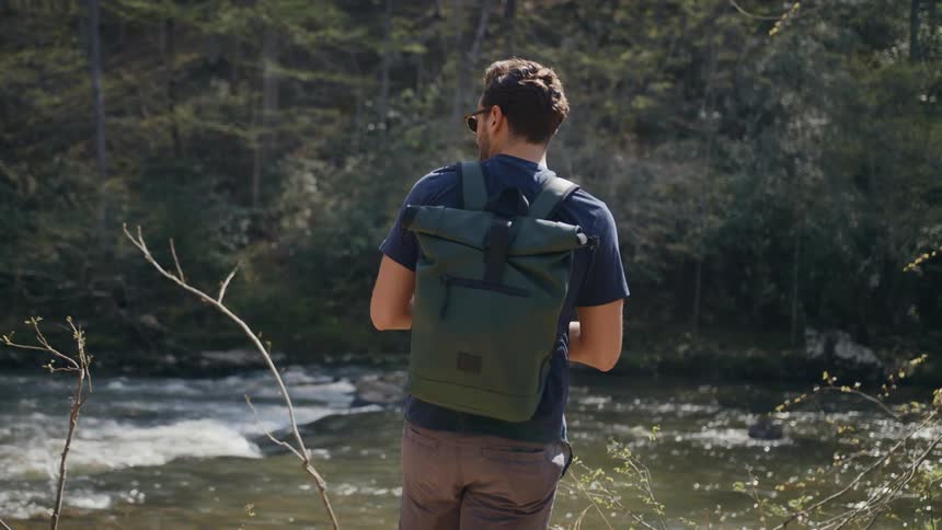 A man stands next to a small river wearing a backpack