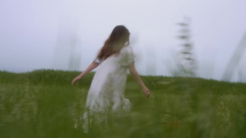 A woman with sunglasses running in a grassy field with the sky and clouds in the background