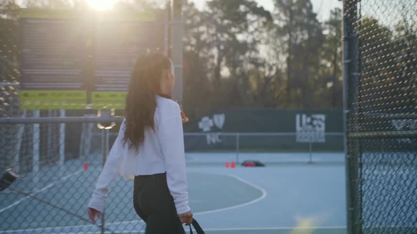 Woman carrying gym bag walks into chain link fence enclosed soccer court
