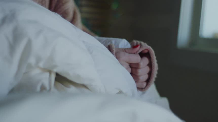 A woman in a room sitting with a wall a plant and a window in the background